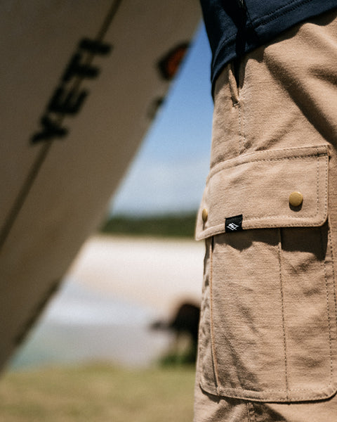 Person wearing a beige jacket with a visible brand logo, standing near a tent outdoors.