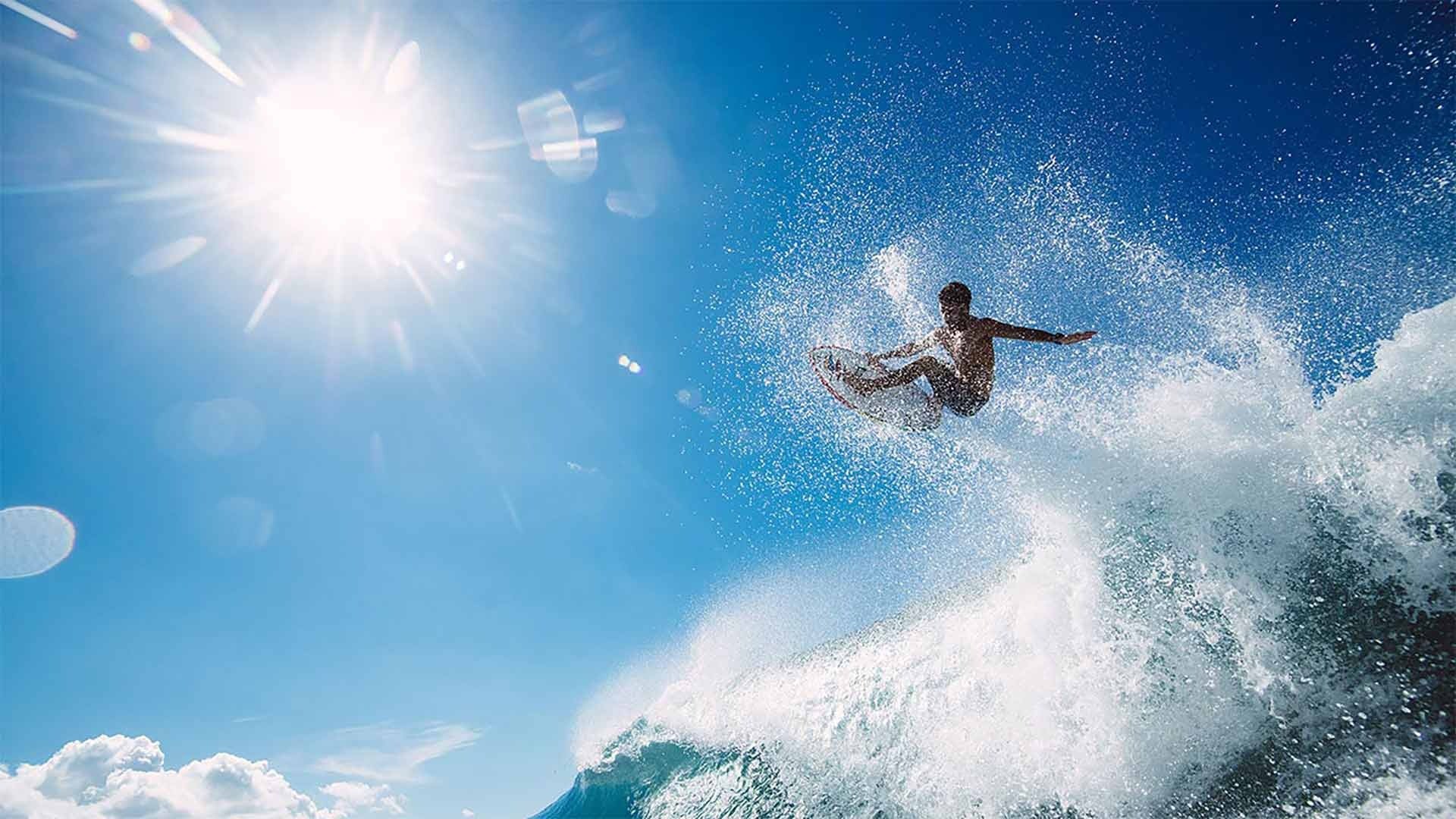 Surfer riding a wave with a bright sun in the background
