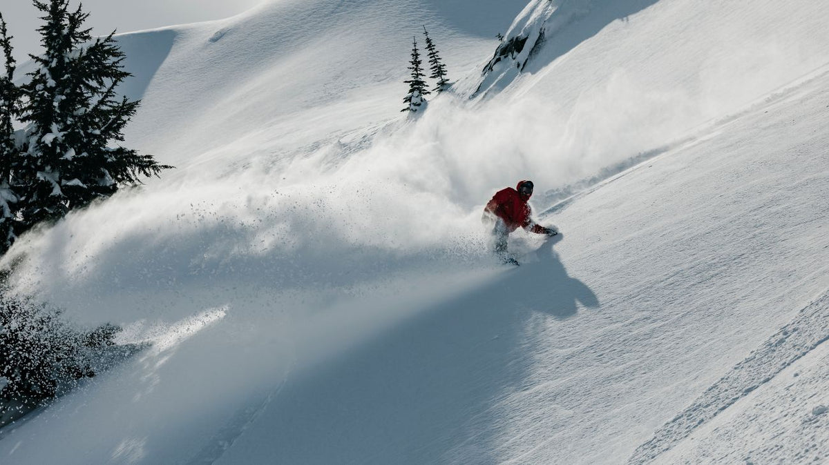 ici on voit le snowboardeur Chris Rasman en pleine action dans la poudreuse, il envoie une gerbe de neige derrière lui.