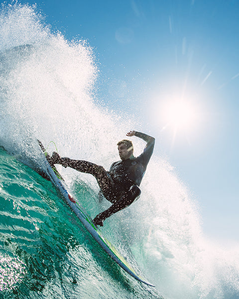 Surfer performing a trick on a wave with clear blue sky