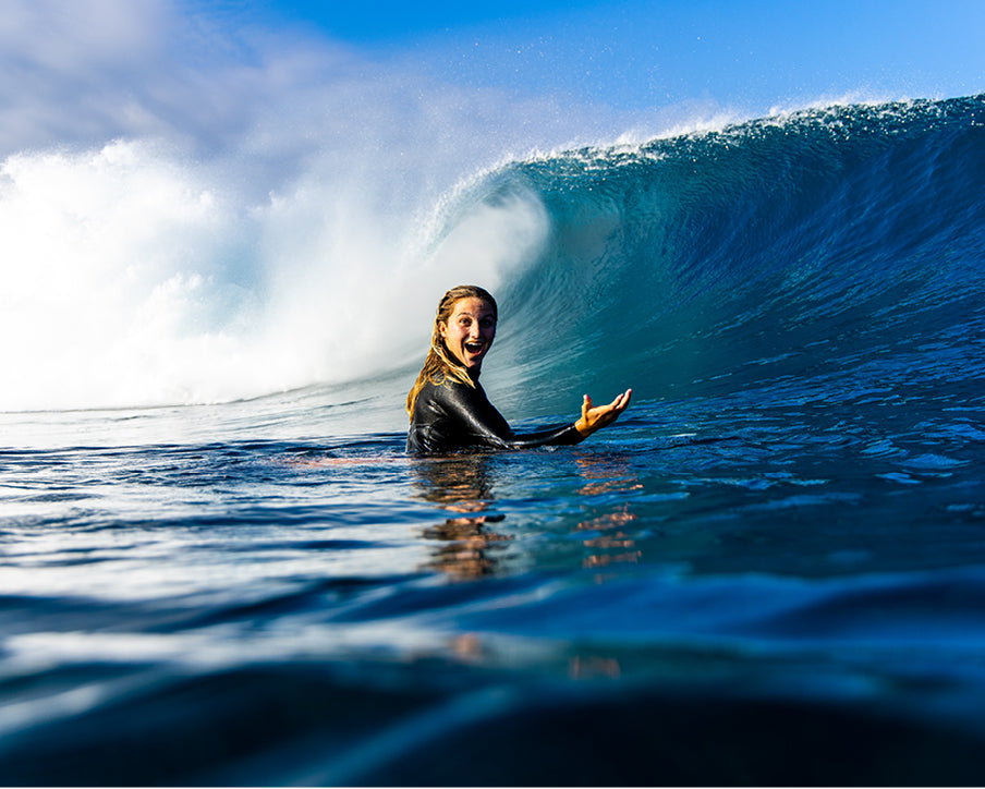 Person in a wetsuit standing in the water with a large wave behind them