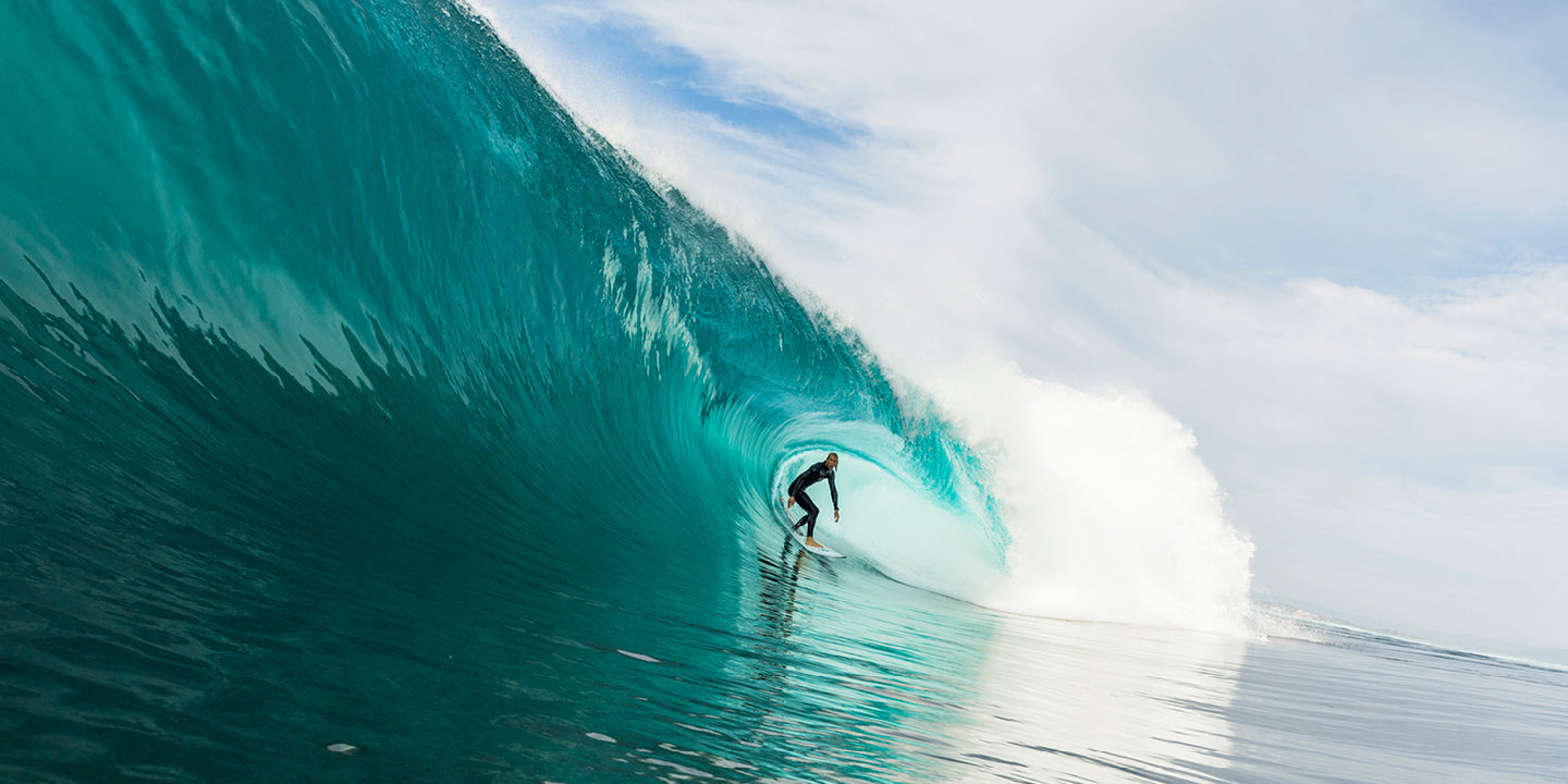 Surfer riding a large wave with a clear sky in the background