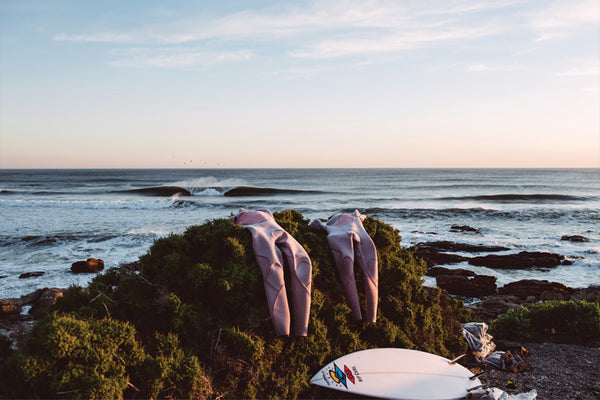 Two pink surfboards on a rocky shore with ocean waves in the background
