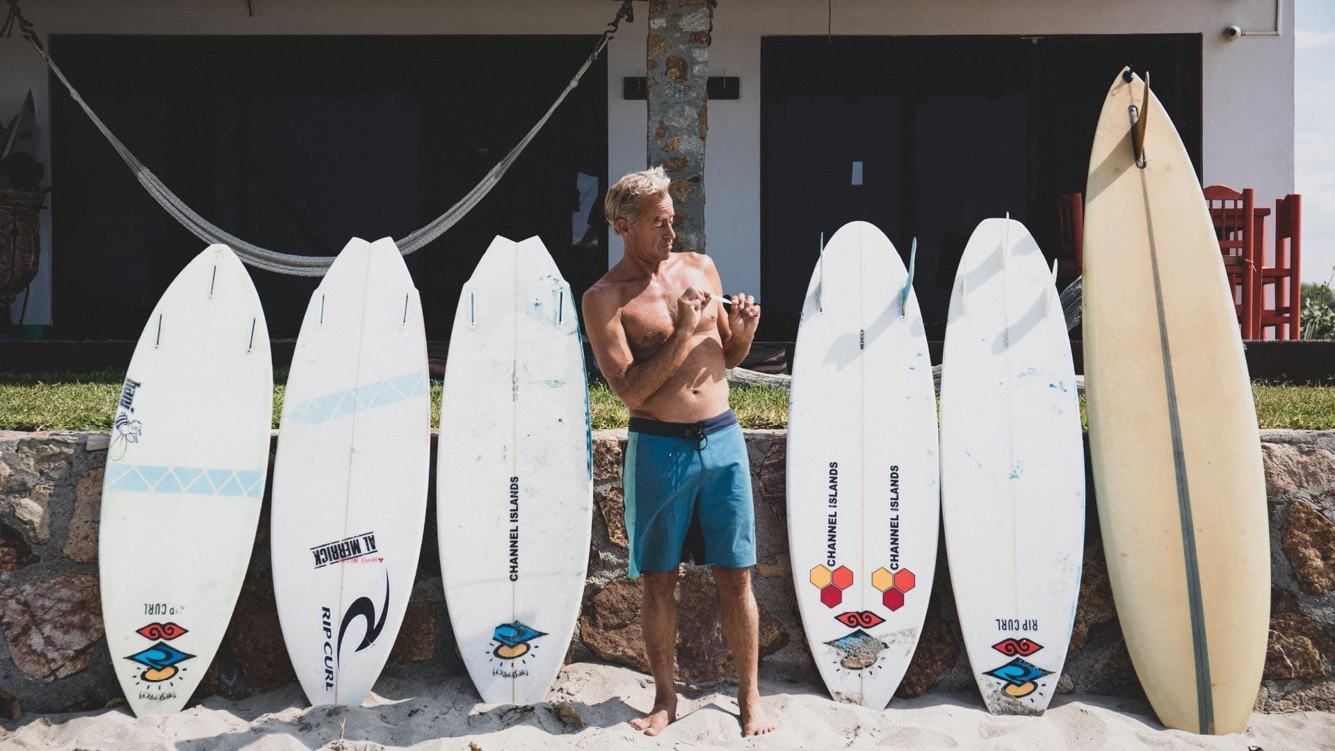 Man standing among six surfboards of various designs on a stone surface.