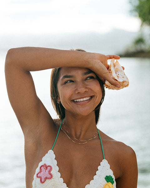 Woman in a floral bikini top holding a shell by the water