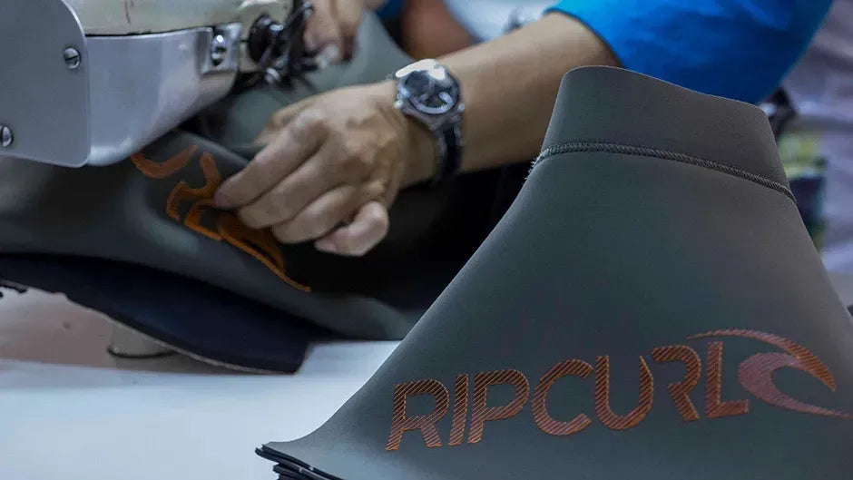 Person working on a sewing machine with a Rip Curl branded item in the foreground.