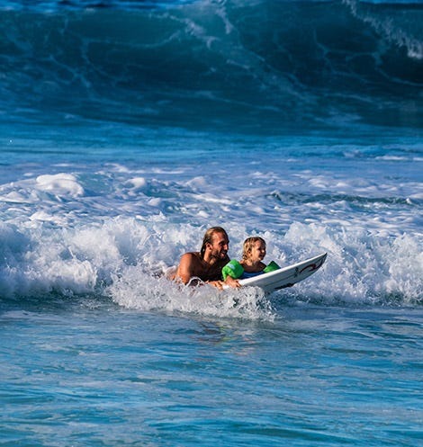 A man surfing with his baby in the foam